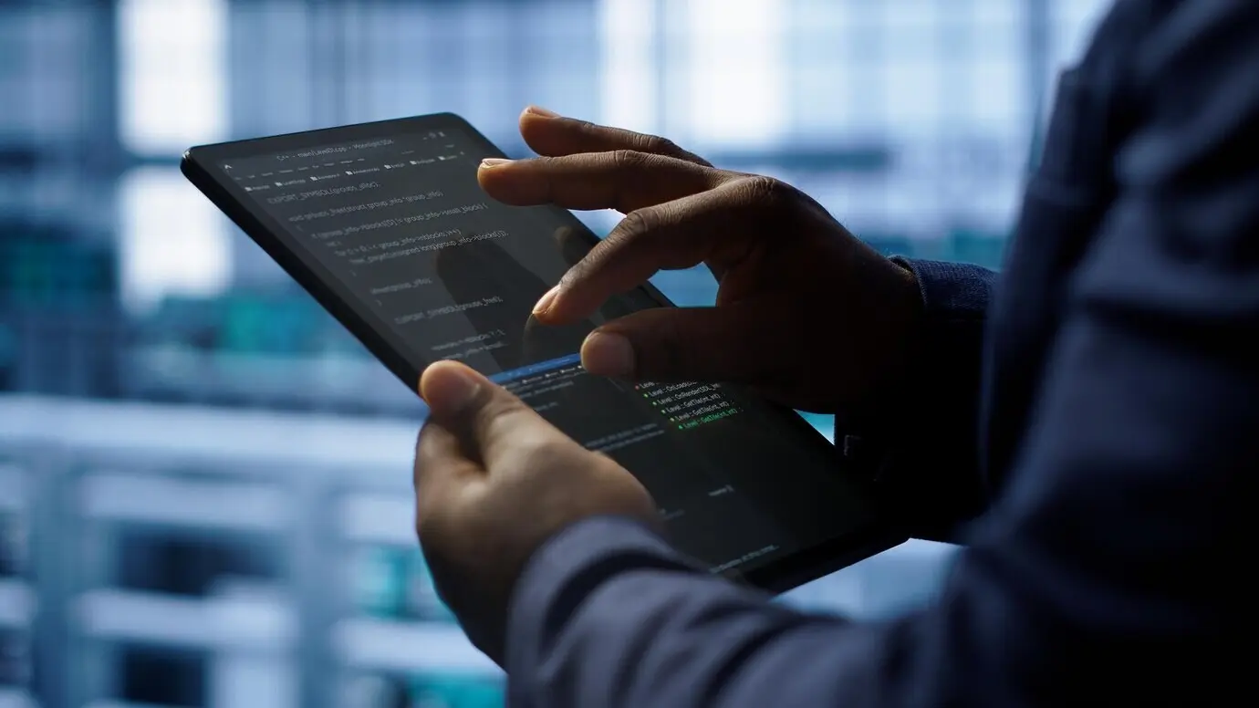 Крупный план работника в серверной, пользующегося планшетом.